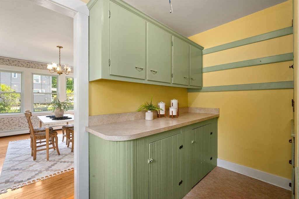 Pantry with sage-green cabinets and beige counter, opening onto a bright dining area.