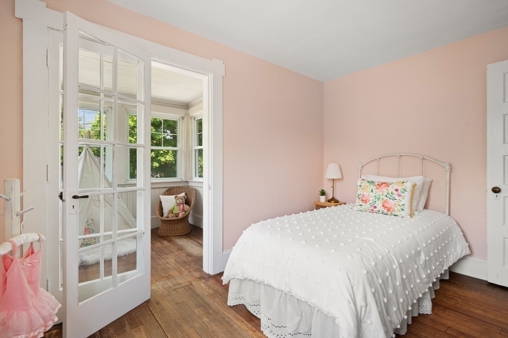 Bedroom with a white bed and pink walls, opening through French doors to a sunny room.