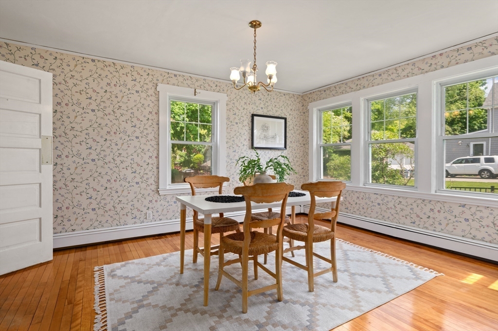 Dining room with floral wallpaper, hardwood floors, and a wooden table beneath a chandelier.