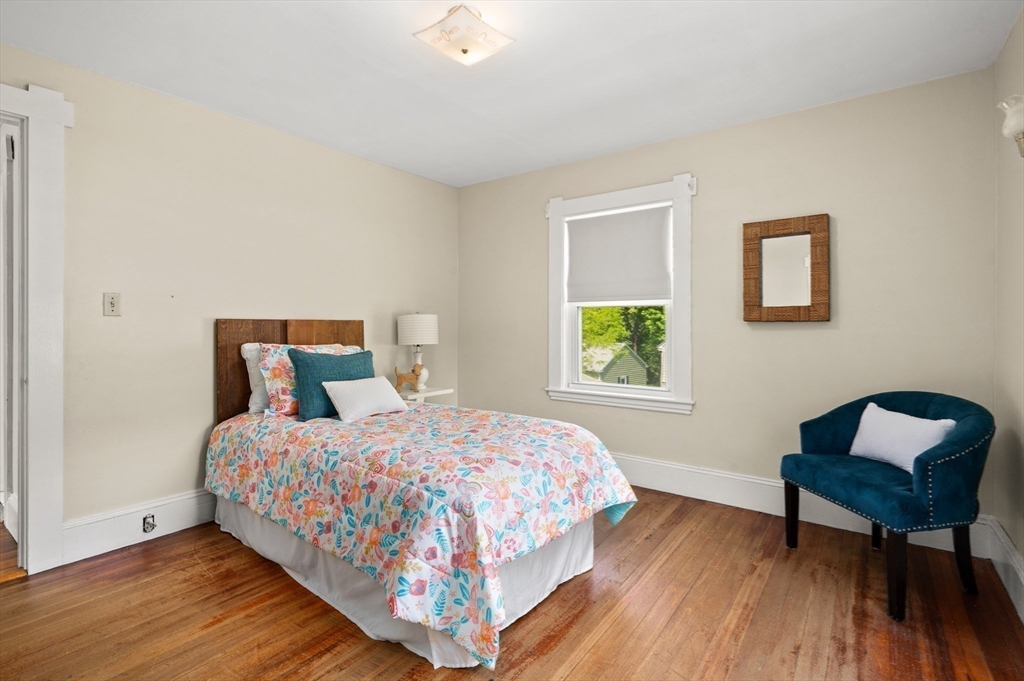 Bedroom with colorful floral bedding, a teal chair, and polished hardwood floors.
