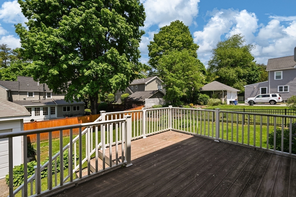 Wooden backyard deck with white railings overlooking a grassy yard and mature trees.