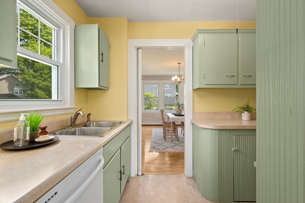 Kitchen with pale green cabinets, yellow walls, a double sink, and a view into the dining room.