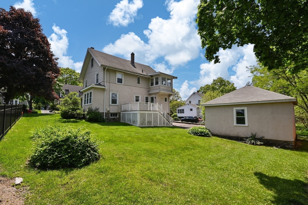 Rear of a two-story home with a raised deck, detached garage, and broad green lawn.