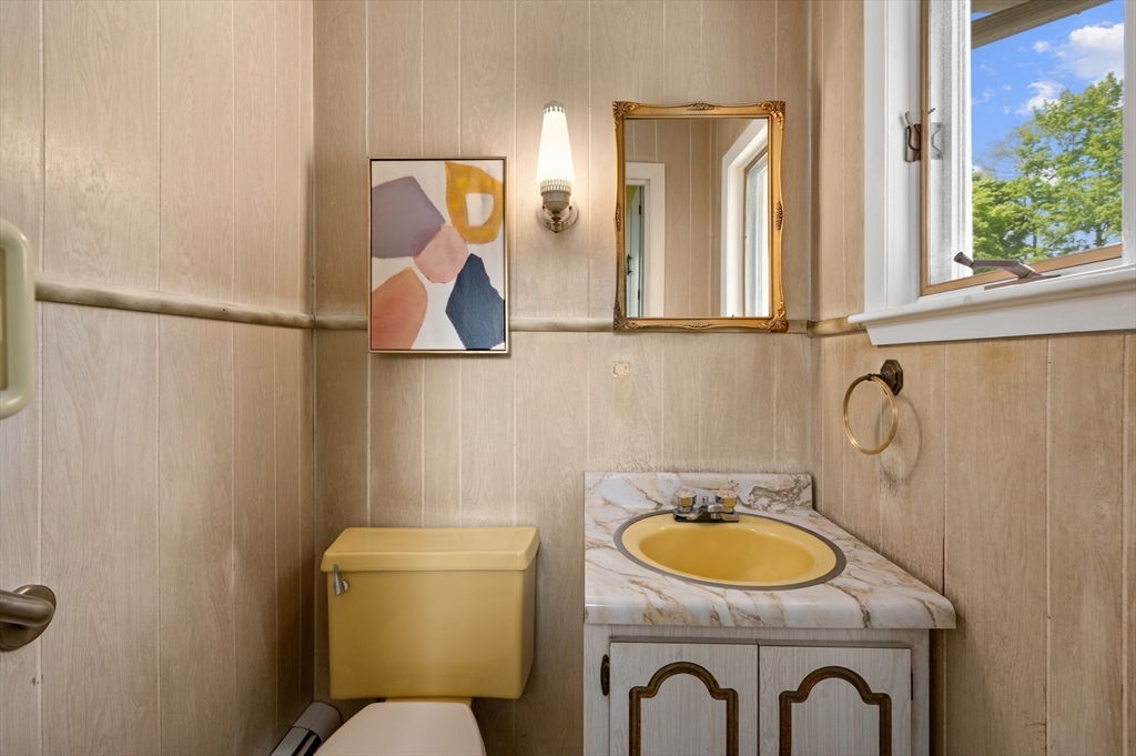 Bathroom with a yellow sink and toilet, marble-look vanity, and window overlooking leafy trees.