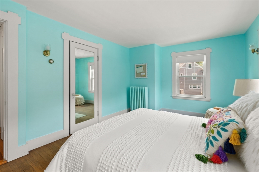 Turquoise bedroom with white trim, a white bed, colorful pillows, and a window.