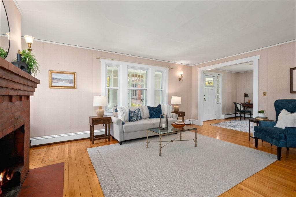Living room with a brick fireplace, hardwood floors, and a light sofa on a large rug.