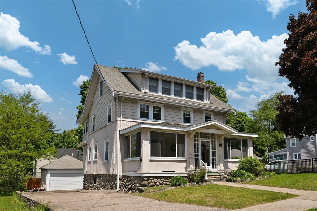 Two-story house with an enclosed sunroom, stone foundation, and detached garage.