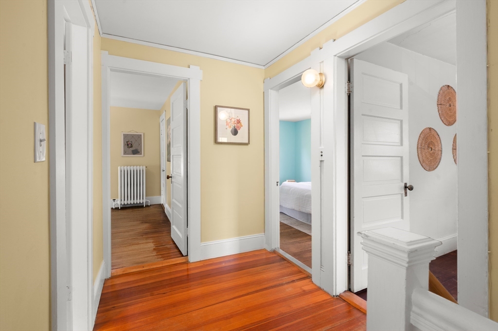 Hallway with polished hardwood floors, pale yellow walls, and open doorways to adjoining rooms.