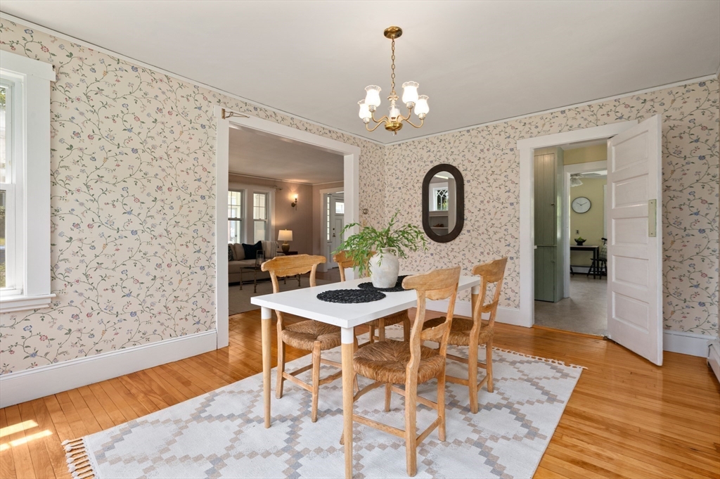 Dining room with floral wallpaper, hardwood floors, and a white table beneath a chandelier.