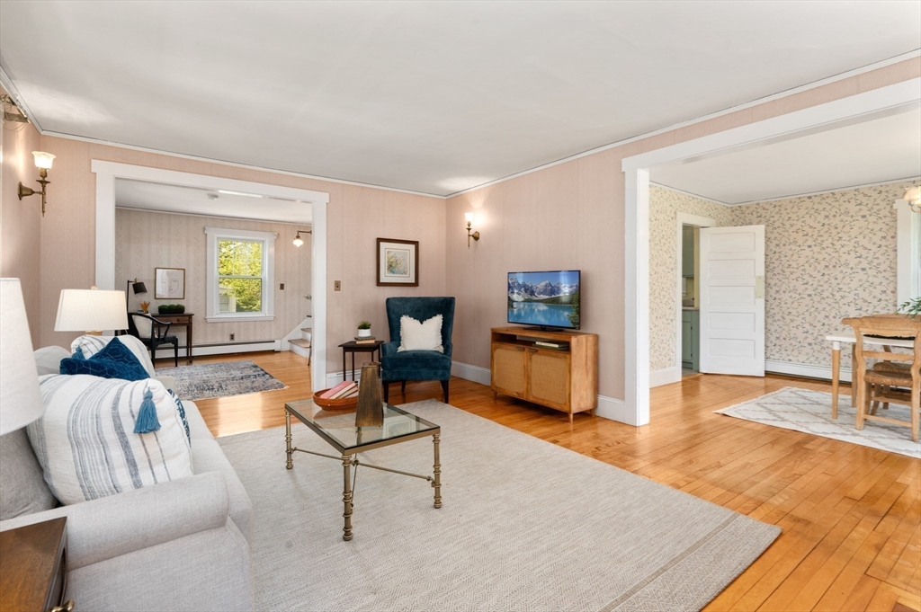 Furnished living room with pale pink walls, hardwood floors, and wide openings to adjoining rooms.