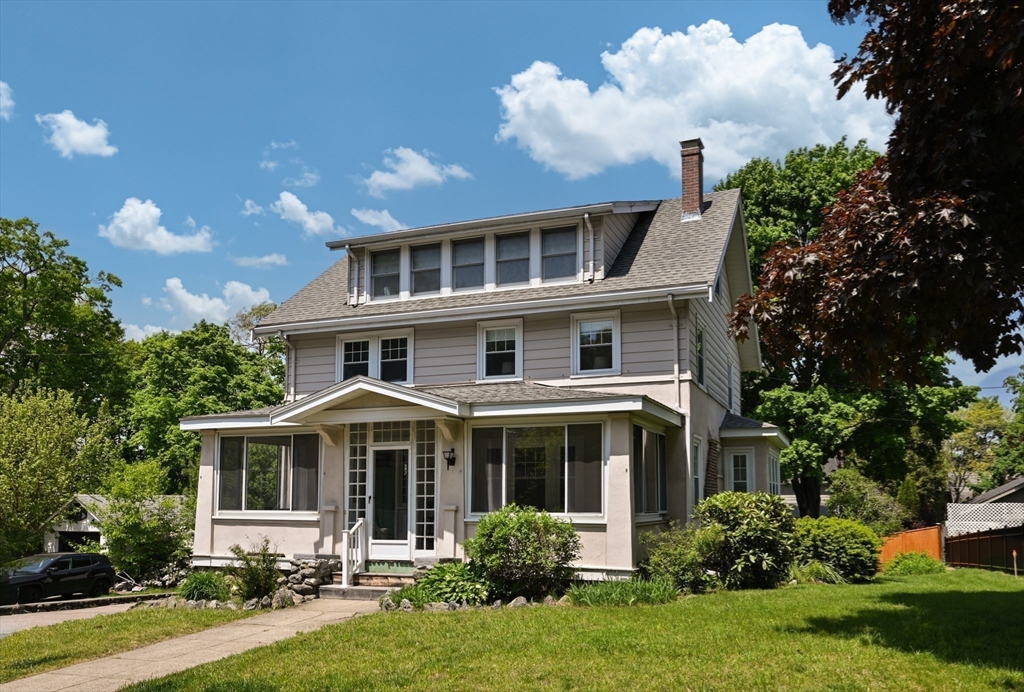 Two-story house with a broad enclosed front porch, dormer, and landscaped lawn.