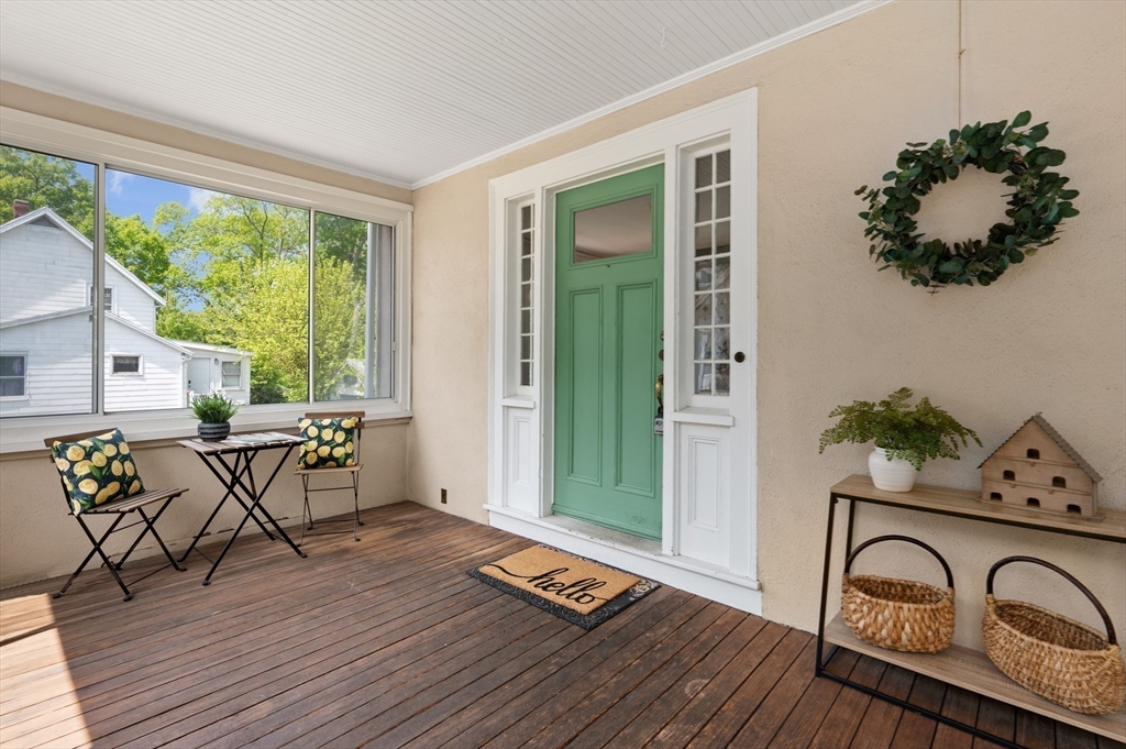 Enclosed front porch with a mint-green entry door, wood decking, and seating beside wide windows.