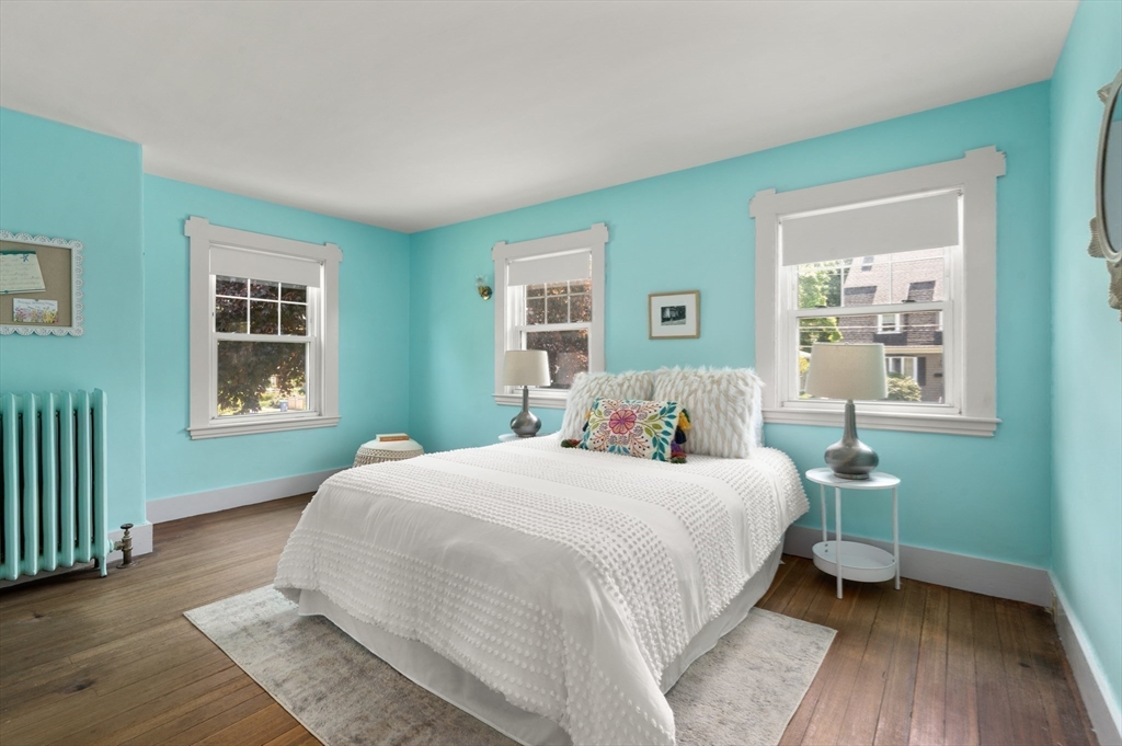Staged bedroom with turquoise walls, three windows, and a white bed with a colorful pillow.