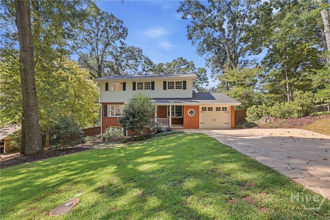 Two-story white-sided and brick home with an attached garage, sloped driveway, and tree-lined lawn.