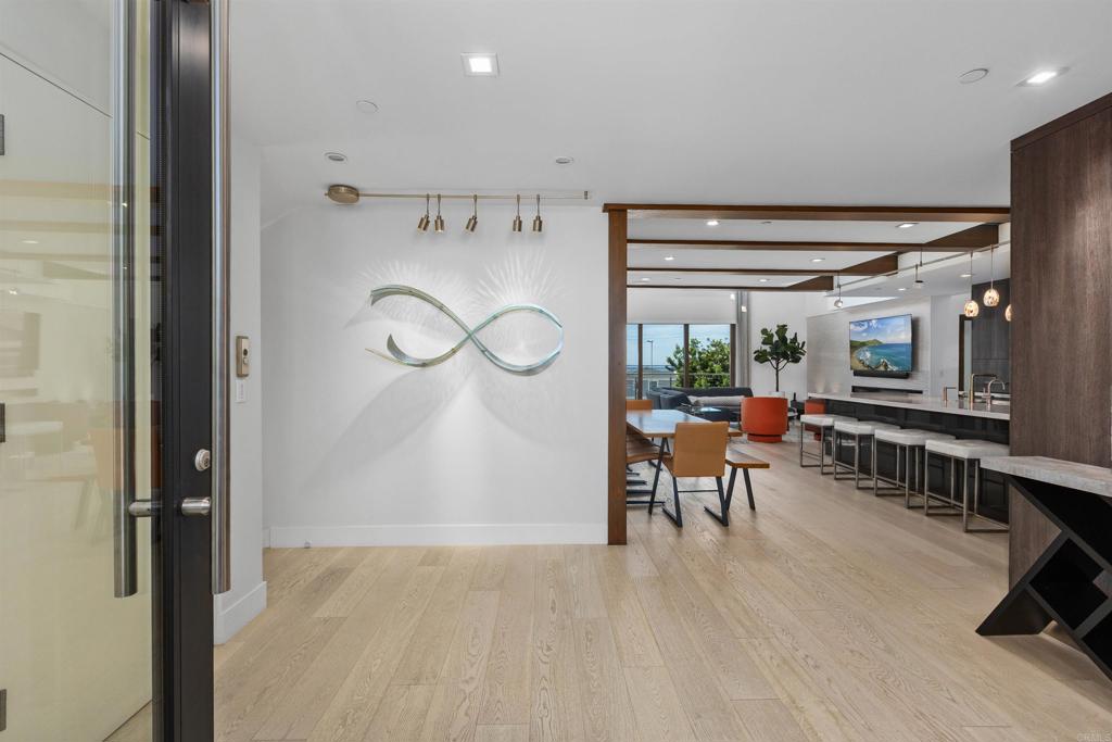 Open-plan living area with pale wood floors, sculptural wall art, and a glimpse of the ocean.