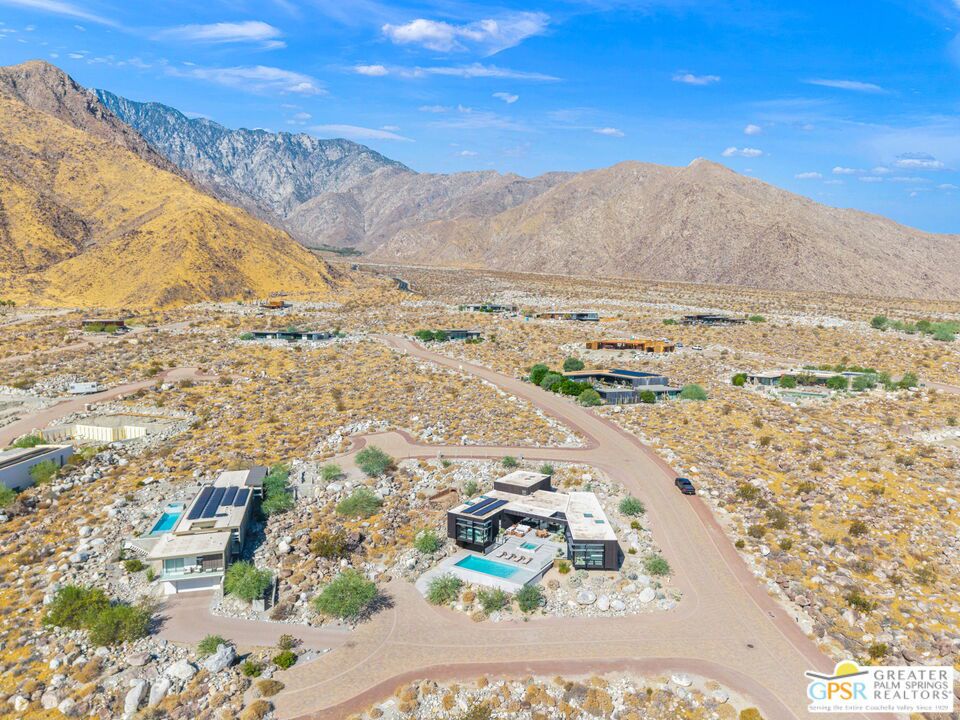 Aerial view of desert homes with pools and rugged mountains behind them.