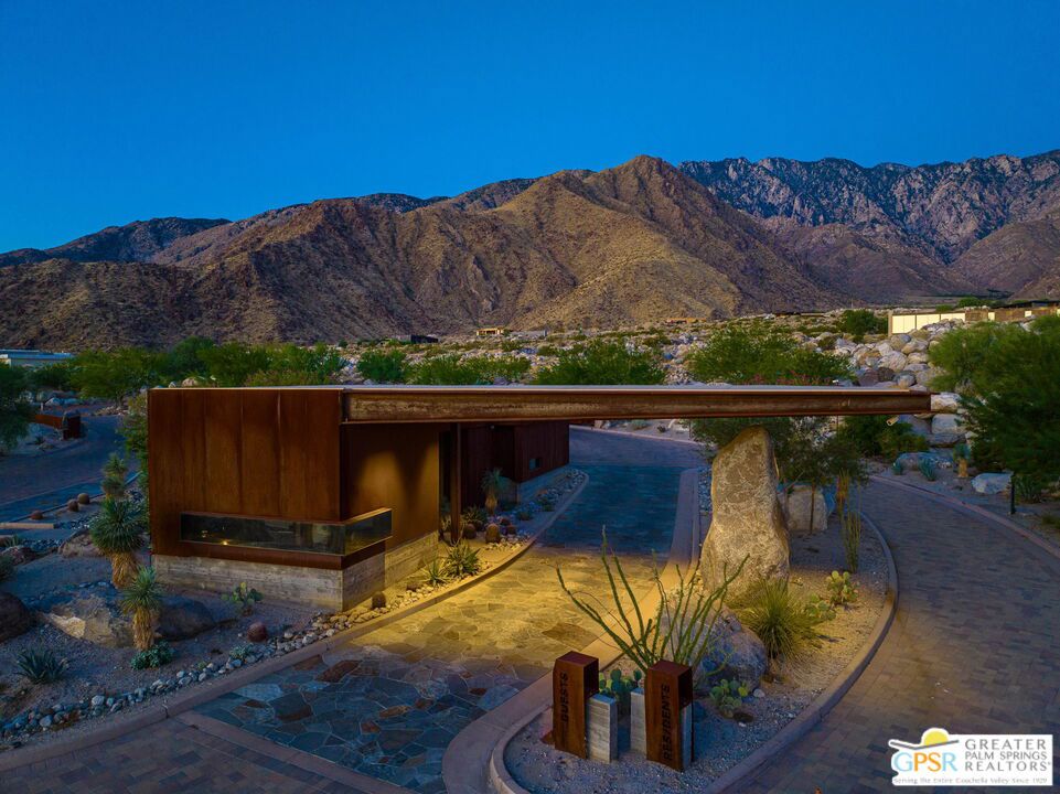 Modern desert home entrance and paved approach, framed by desert landscaping and the San Jacinto Mountains at dusk.