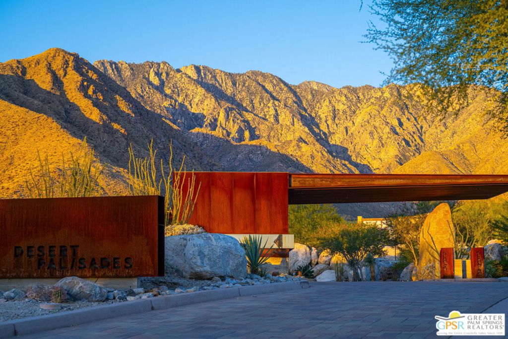 Desert Palisades community entrance with a rust-colored monument sign and sunlit mountains.