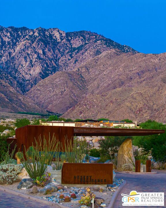 Palm Springs property entrance with a rust-colored modern gate, desert landscaping, and mountains behind it.