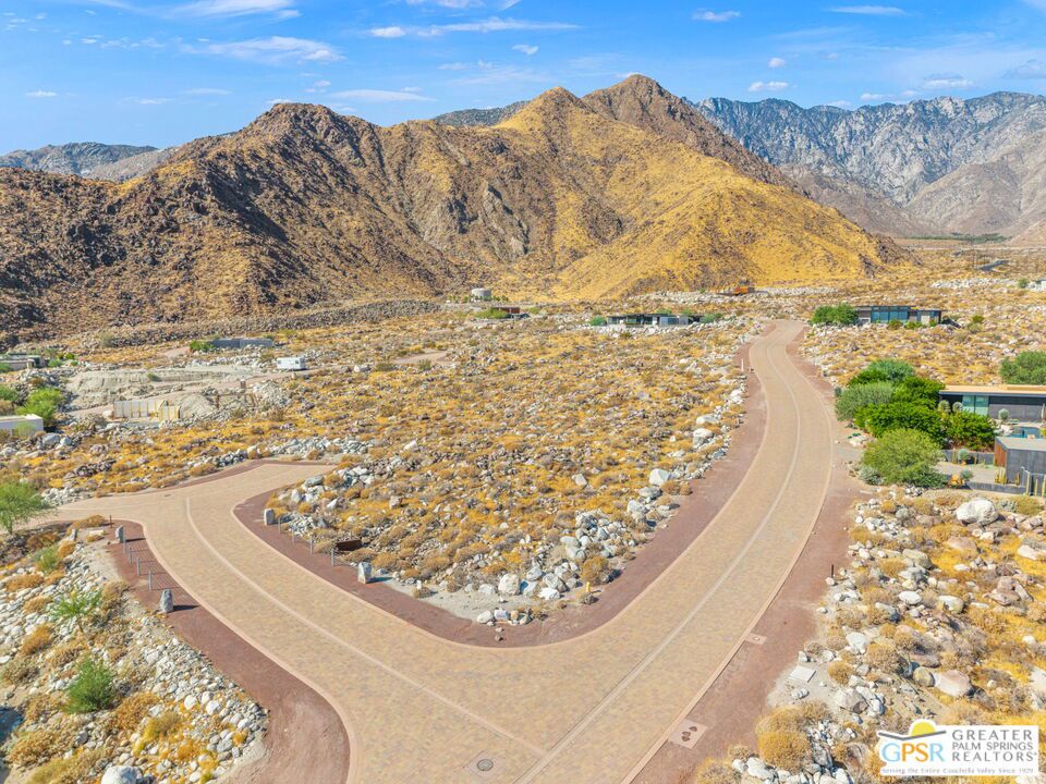 Aerial view of a desert neighborhood street curving toward rugged mountains.