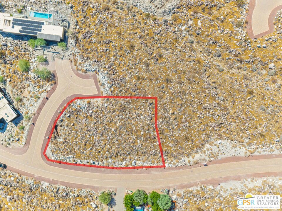 Vacant rocky desert lot outlined in red beside a curving paved road.
