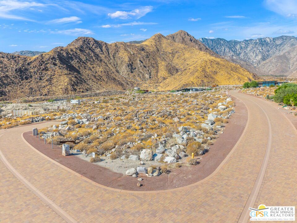 Curving paved roadway borders desert landscaping, with rugged mountains in the background.