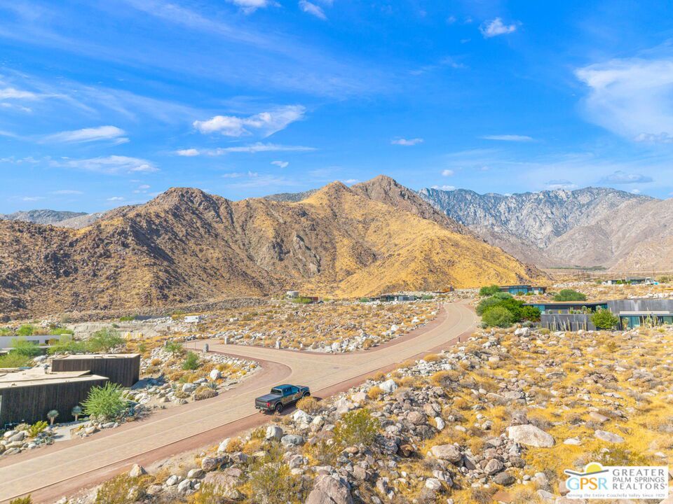 Aerial view of desert homes along a curving road beneath the surrounding mountains.