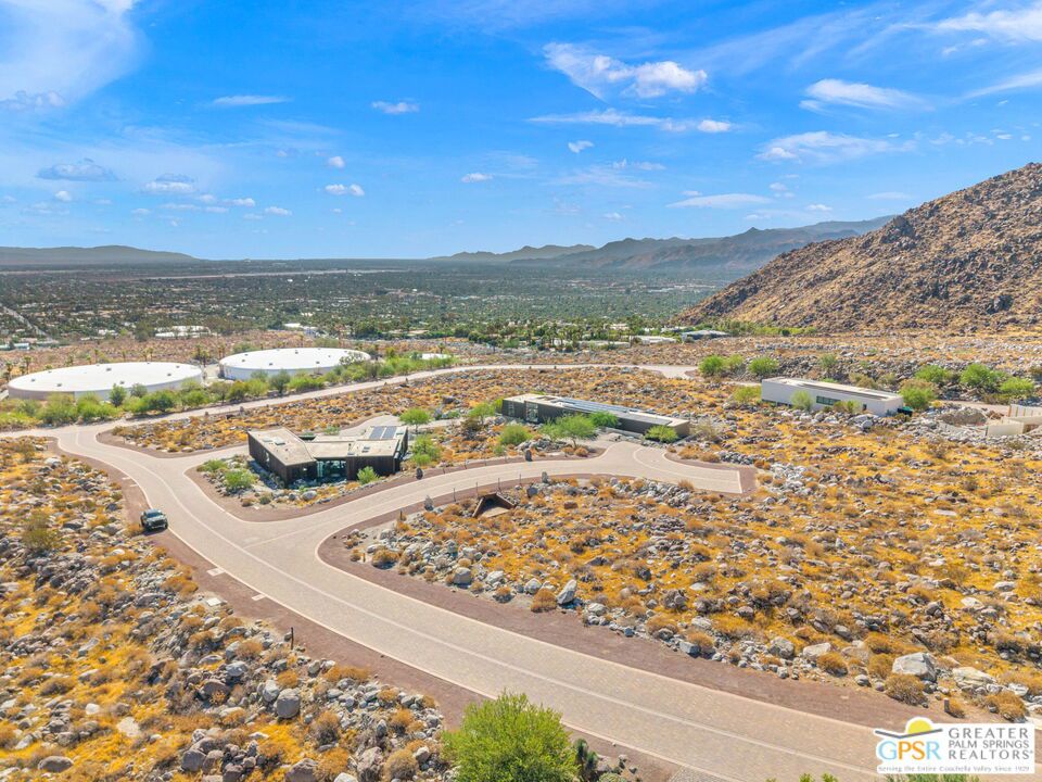 Aerial view of modern desert homes on a rocky hillside, with the valley and mountains in the distance.