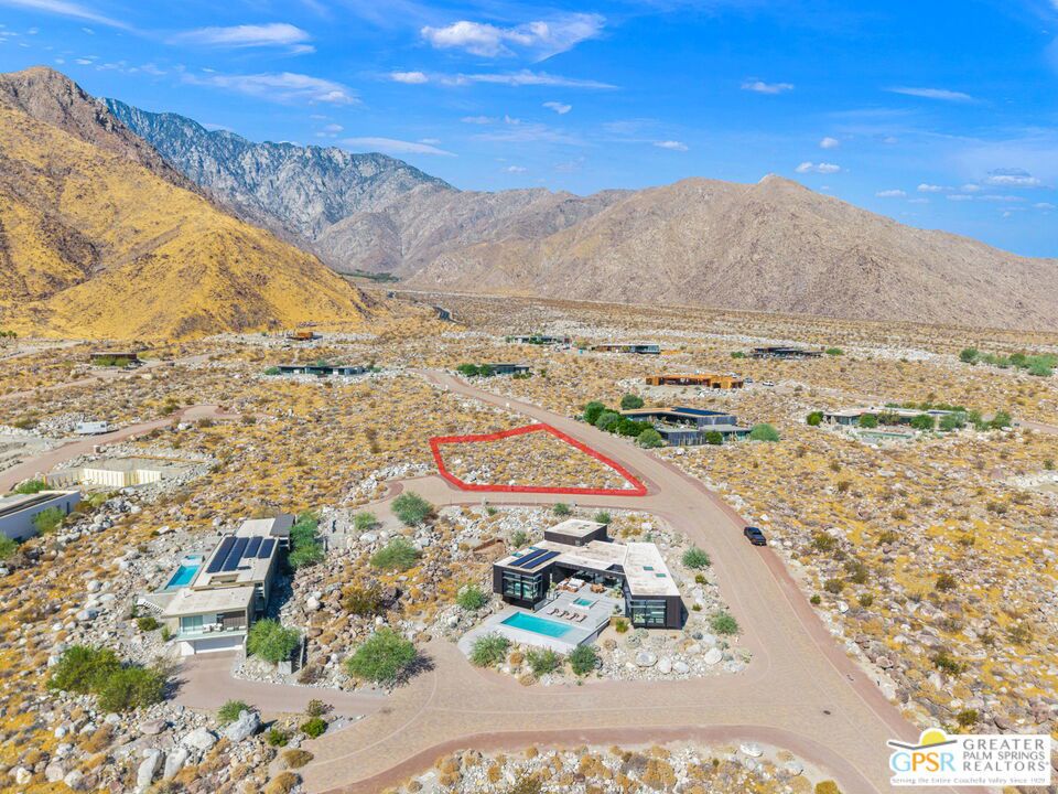 Aerial view of a red-outlined desert lot among modern homes, rocky terrain, and Palm Springs mountains.