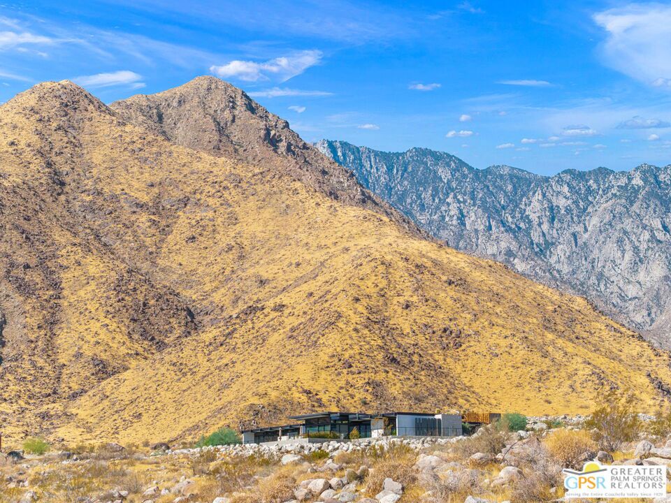 Modern desert home beneath golden mountain slopes and a bright blue sky.