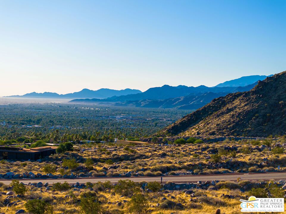 Desert valley and mountain panorama with scrubland and a rocky hillside in the foreground.