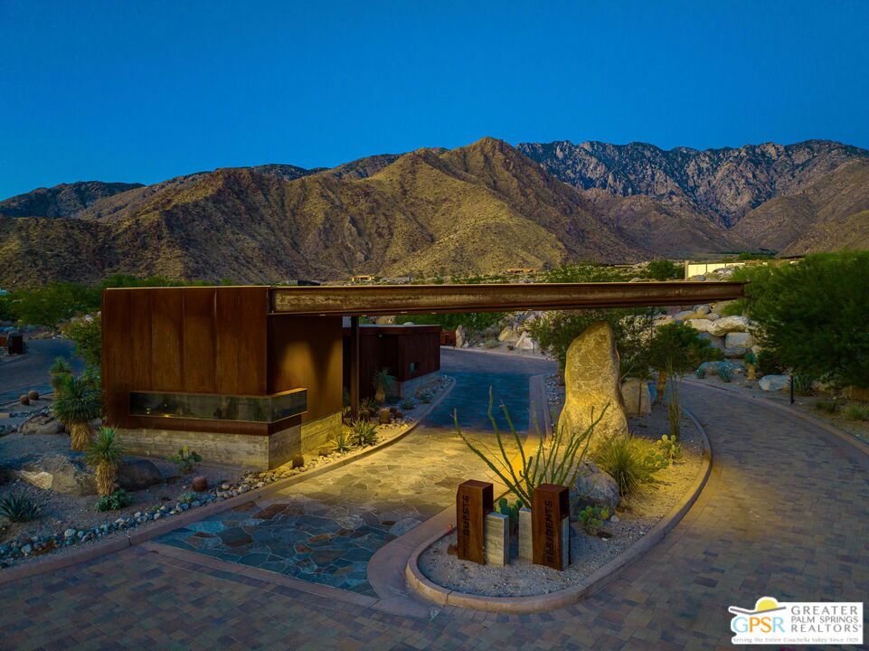 Modern desert home entrance with a rust-colored gate structure and mountains behind it.