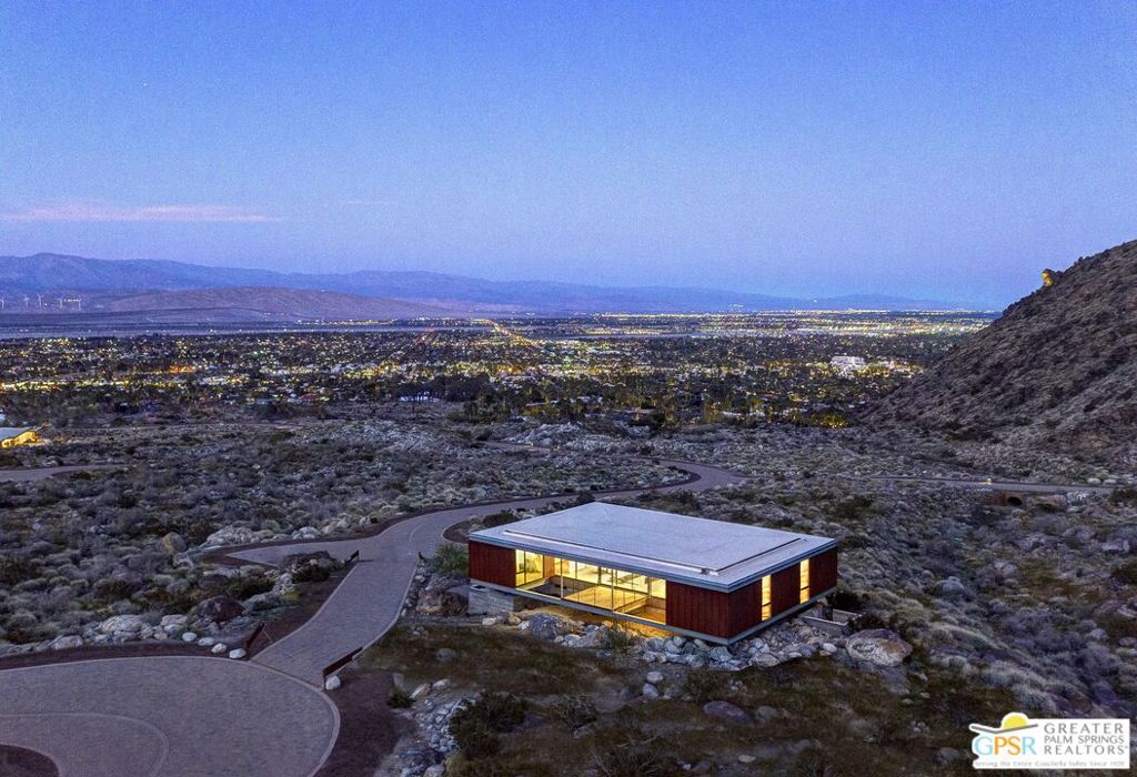 Modern desert home with glowing windows above Palm Springs, with valley lights and mountains beyond.