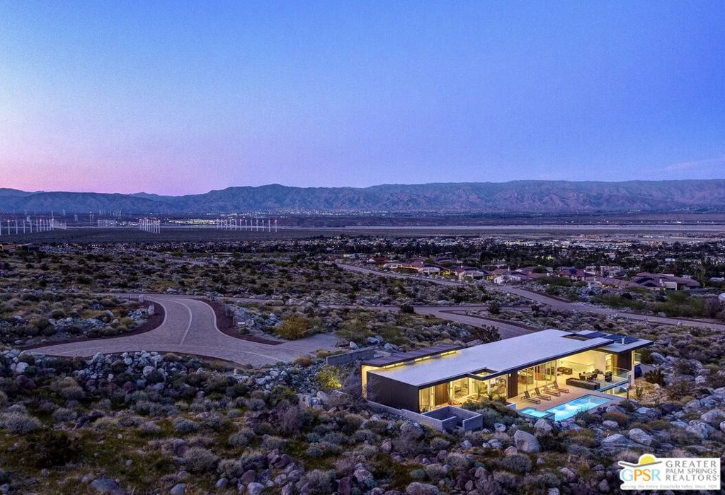 Aerial view of a modern desert home and pool at dusk, with mountains beyond.