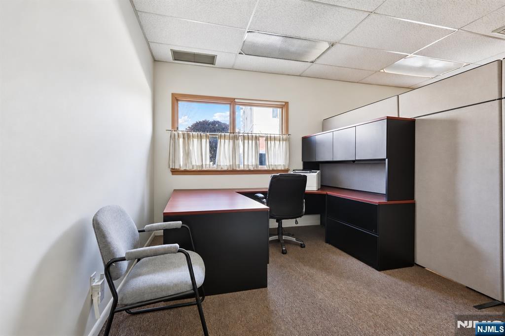 Office with dark desks and cabinets, a guest chair, and a curtained window.