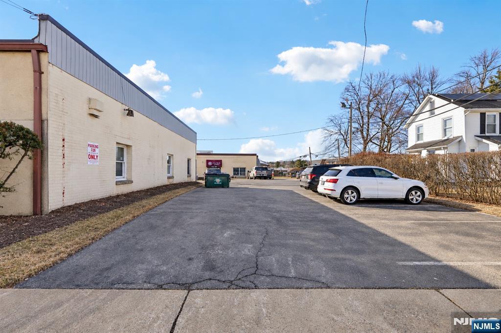 Commercial building beside a paved parking lot with parked cars and a neighboring house.