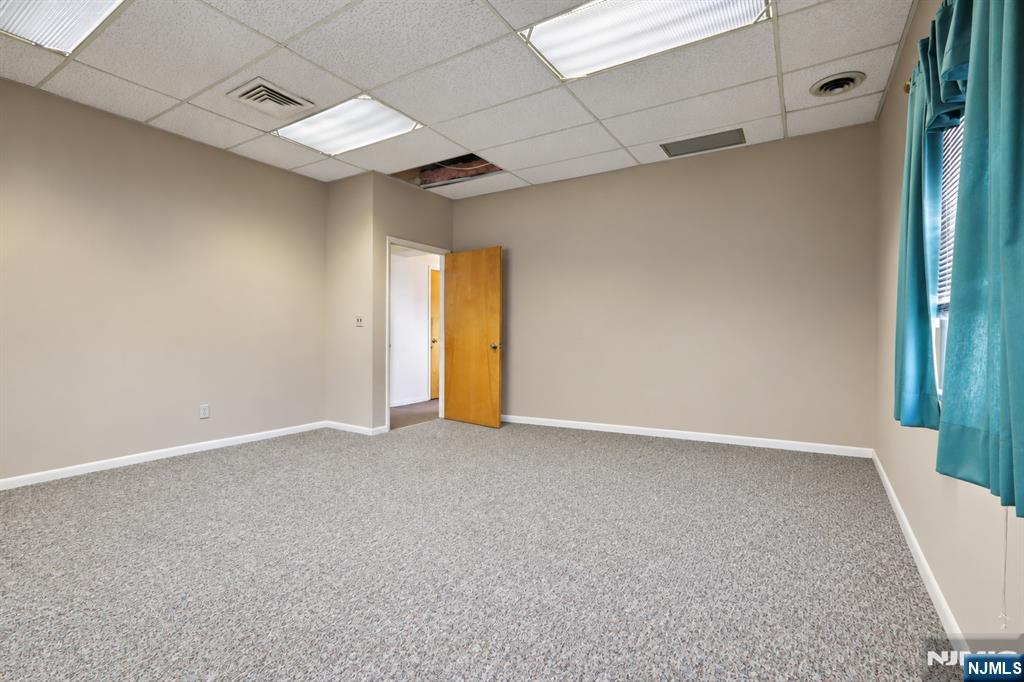 Empty carpeted room with teal curtains, an open wooden door, and a suspended ceiling.