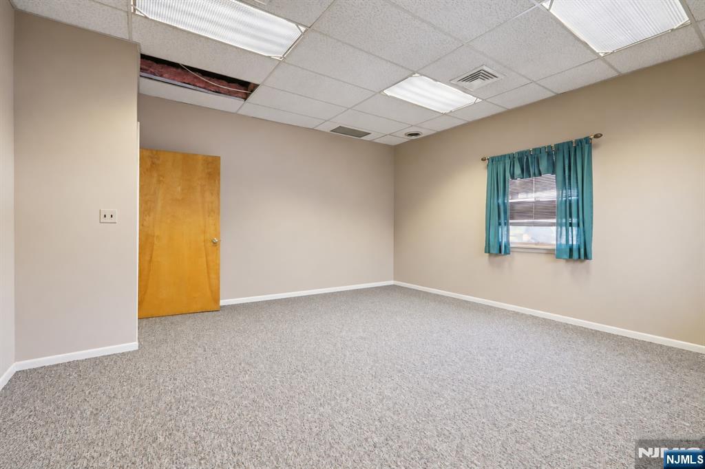 Empty carpeted room with teal curtains, a wooden door, and a missing ceiling tile.