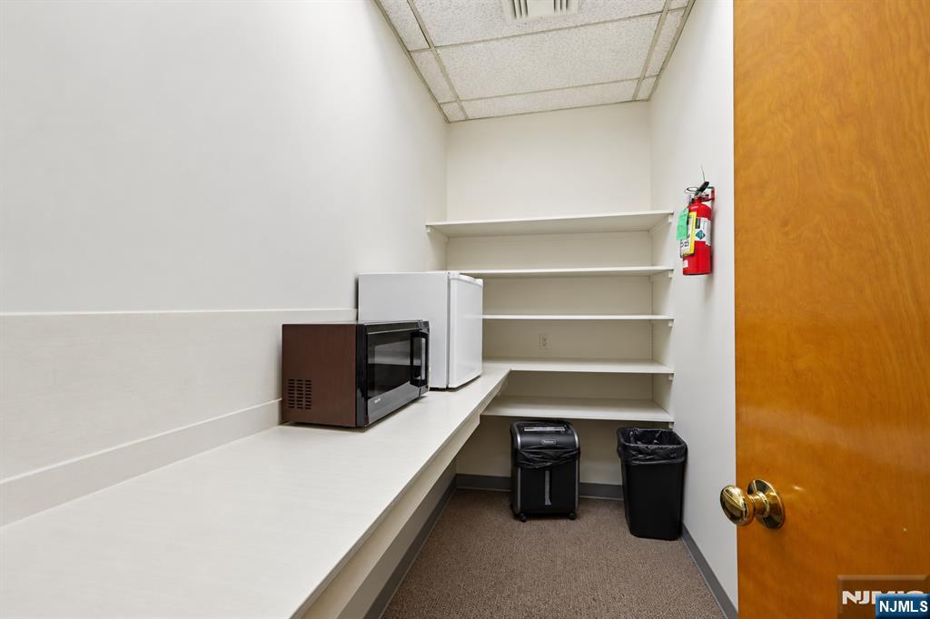 Break room with a long countertop, microwave, compact refrigerator, and open shelves.