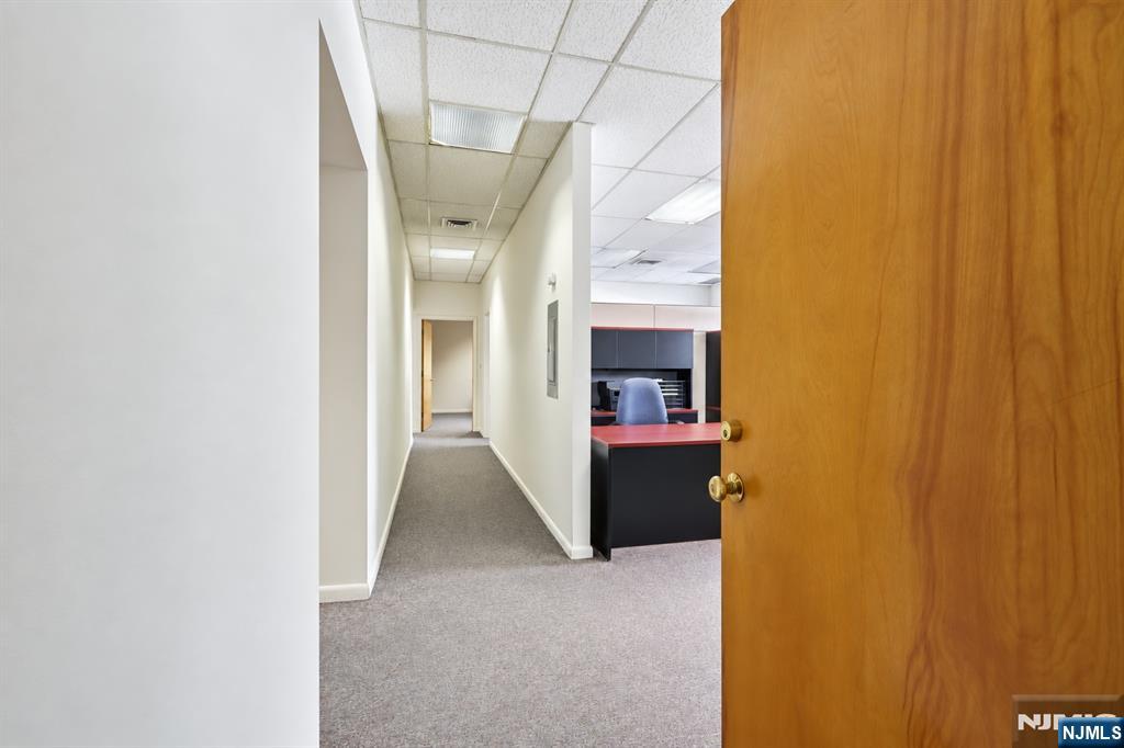 Office hallway leading to a reception desk, viewed through an open wooden door.
