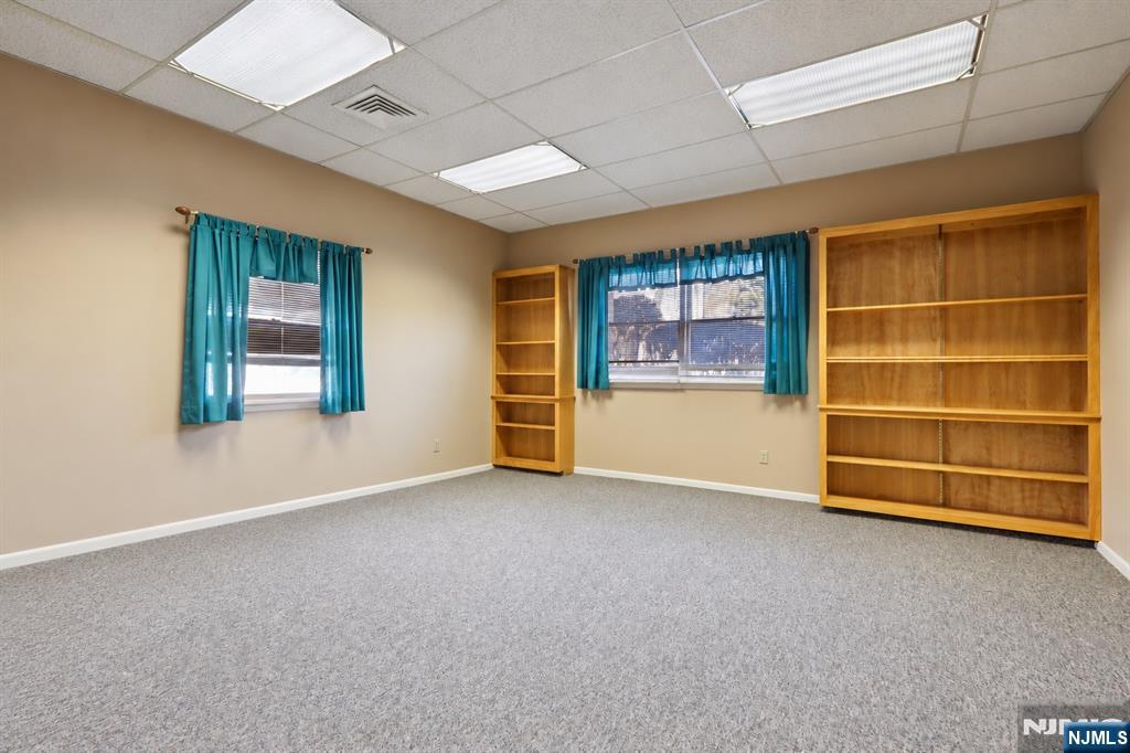 Vacant carpeted office with teal-curtained windows and built-in wooden bookshelves.