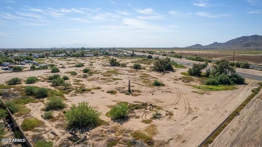 Aerial view of a vacant desert parcel with sparse shrubs, bordering road, and distant mountains.
