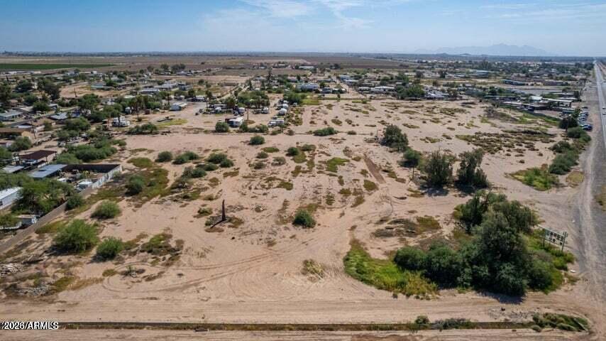 Aerial view of vacant sandy land with desert scrub, nearby homes, and a road along its edge.