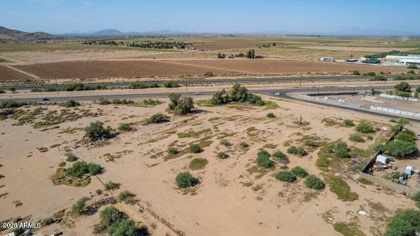 Aerial view of a vacant desert lot beside a highway, with farmland and distant mountains.