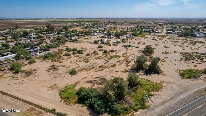 Aerial view of vacant desert lot beside a road, with scattered homes and scrub.