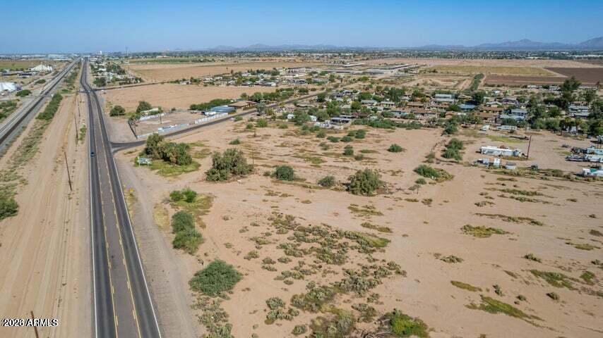 Aerial view of open desert land beside a highway, with scattered homes and distant mountains.