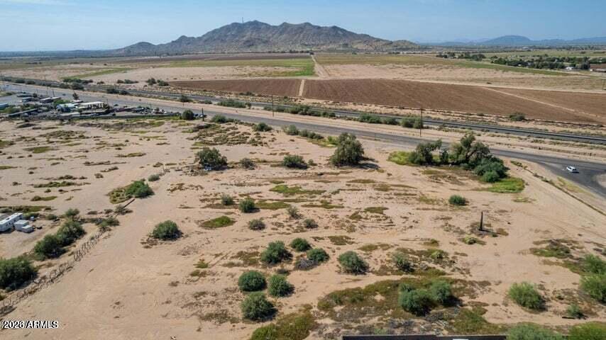 Vacant desert property with sparse shrubs, a road, fields, and mountains in the distance.