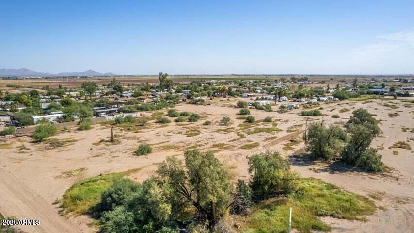 Aerial view of a dry vacant lot with scattered trees and nearby homes.
