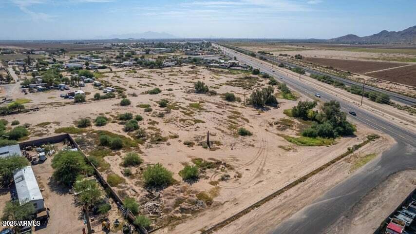 Aerial view of a scrub-covered vacant parcel beside a road, with a highway and distant mountains.