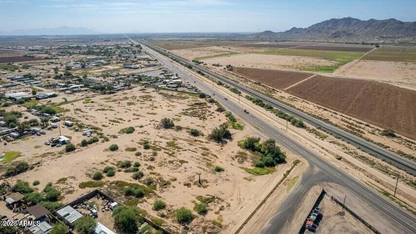 Aerial view of sandy desert land beside a highway, with scattered homes and distant mountains.